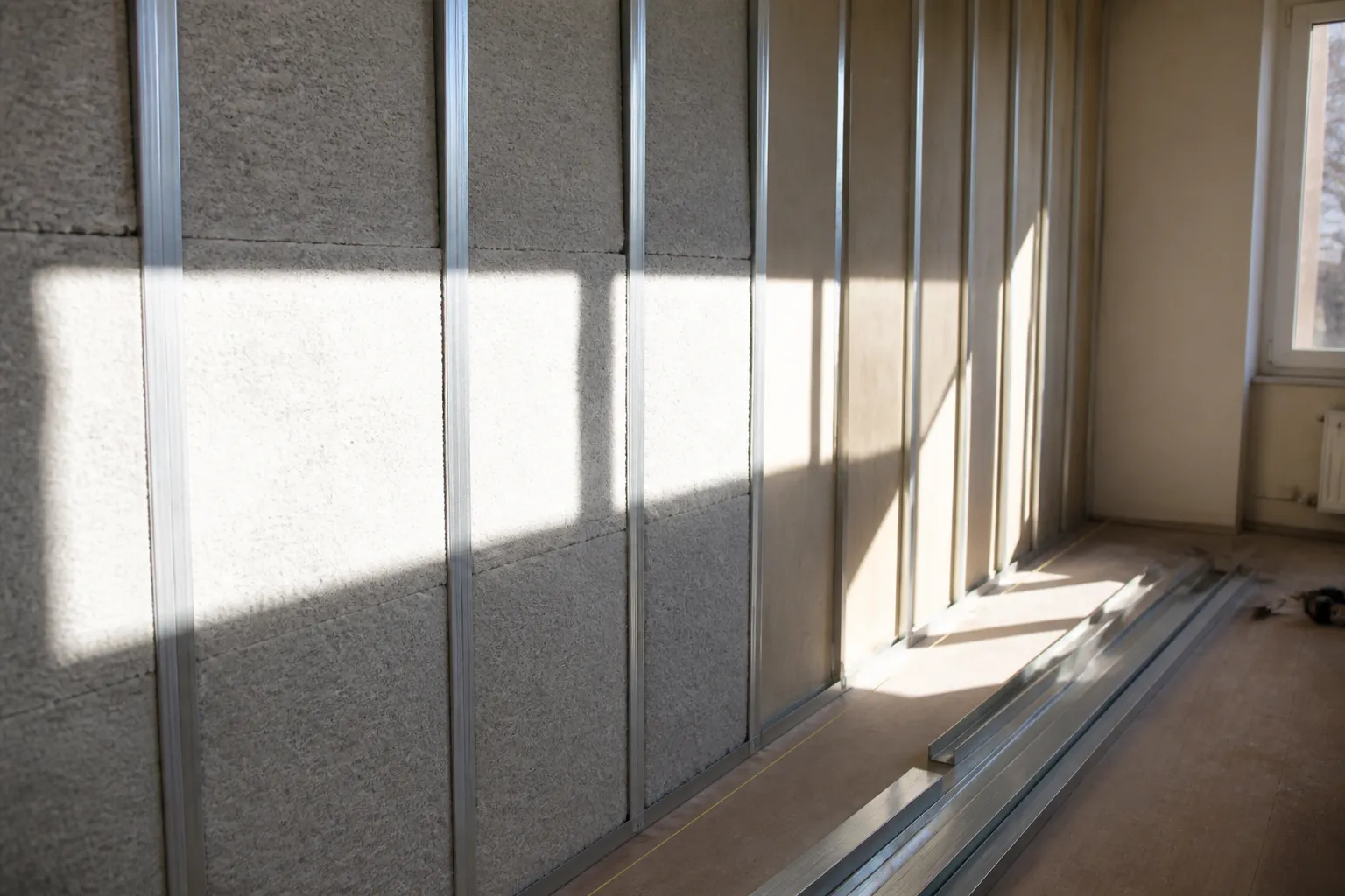 Doublage intérieur en cours de pose, ossature et panneaux isolants sur une moitié du mur, maçonnerie nue sur l’autre
