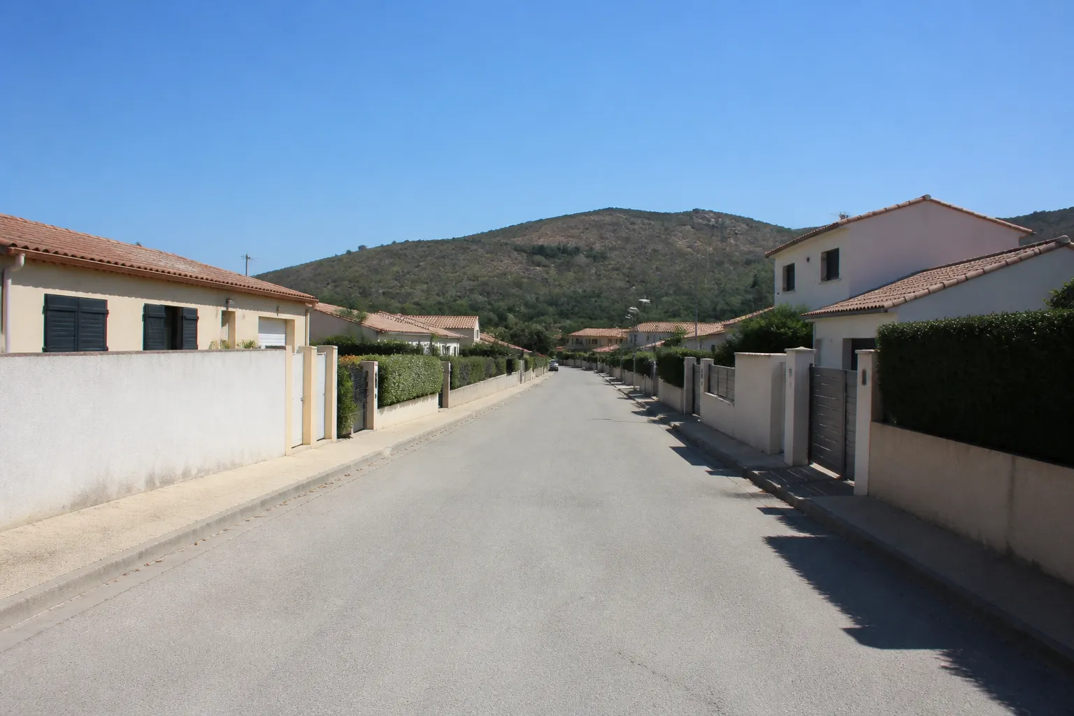 Rue de lotissement varois, maisons individuelles d’époques différentes, toitures de tuiles et colline sèche en fond
