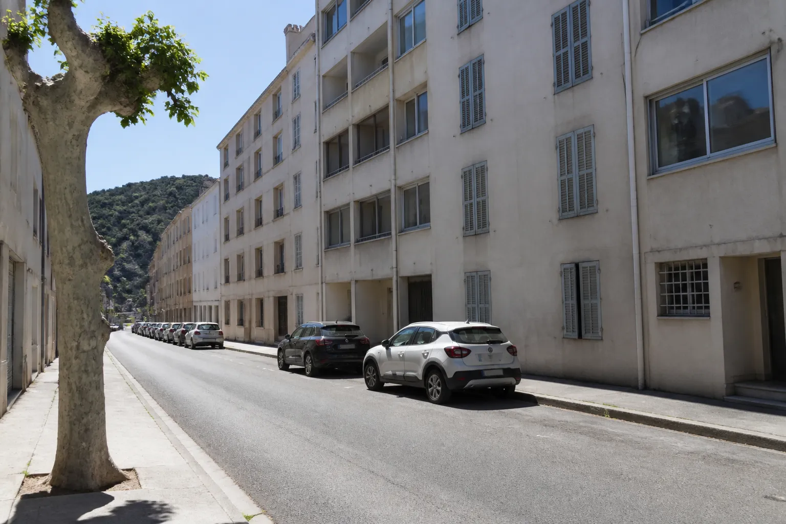 Rue de ville méditerranéenne, immeubles d’habitation mitoyens de quatre à six niveaux, volets pleins et persiennes en façade